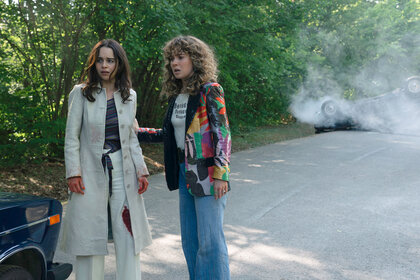Bea and Twila standing outside by a car and smoke behind them in PONIES Season 1 Episode 8.