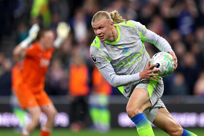 Erling Haaland holding a soccer ball while running on a soccer field.