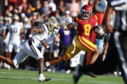 King Miller #8 of the USC Trojans runs with the football as a Washington Huskies defender reaches out during a college football game.