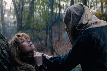 Linda Cardellini as Pam Voorhees leans against a tree in a forest while Zachary Branch as Adult Jason Voorhees grabs Pam Voorhees by the neck with a sack covering the face.
