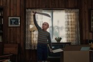 Callum Vinson as Jason Voorhees stands in a wood-paneled room holding a large machete overhead beside moving boxes and a television.