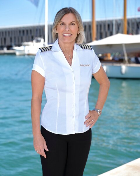 Captain Sandy Yawn smiling in her uniform in front of a marina.