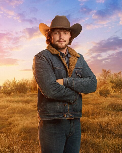 Brayden McBee standing in front of a farm field, trees, and dusk skies.