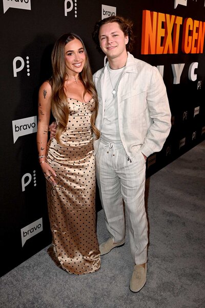 A woman in a light brown satin dress with black polka dots posing with a man wearing all cream clothing