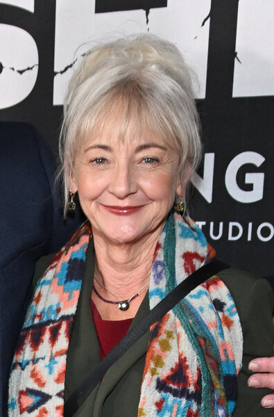 Bonita Friedericy smiles at the camera while posing on a red carpet in front of a black and white backdrop.