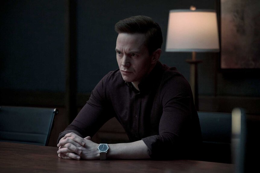 Cobb sitting at a desk with his hands folded in The Copenhagen Test Season 1 Episode 3.