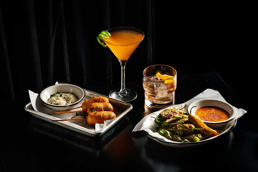Various food items and drinks against a black curtain for The Traitors viewing party at Black Tap.