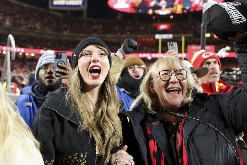 Taylor Swift and Donna Kelce stand together cheering at a football game.