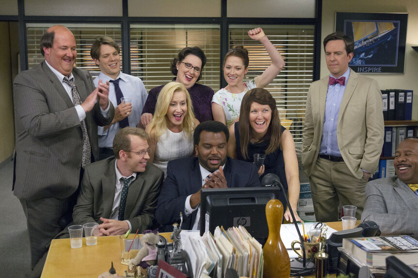 The cast of The Office Season 9 cheering at a desk in The Office Season 9.