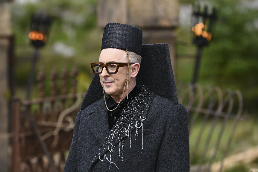 Alan Cumming standing outdoors in a grey outfit in The Traitors Season 4 Episode 1.