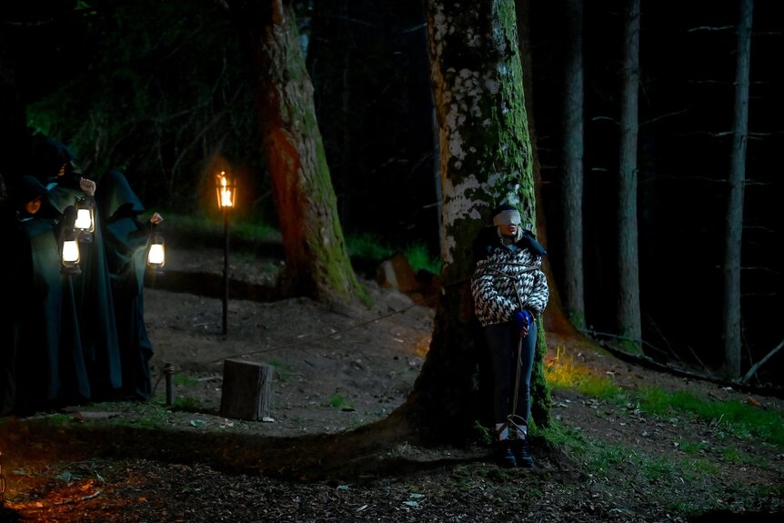 Caroline Stanbury stands blindfolded near a tree in the dark as hooded figures approach on The Traitors Episode 403.