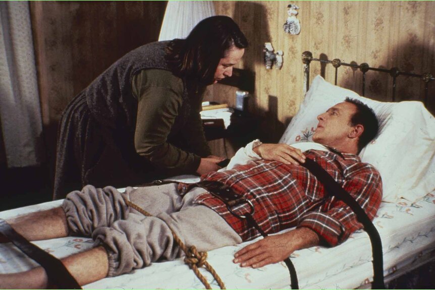 Annie Wilkes (Kathy Bates) straps Paul Sheldon (James Caan) onto a bed on Misery (1990).