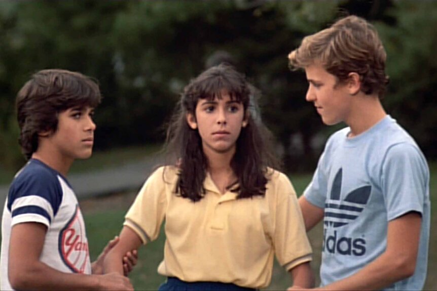Two boys hold onto a girl in a yellow shirt on Sleepaway Camp (1983).