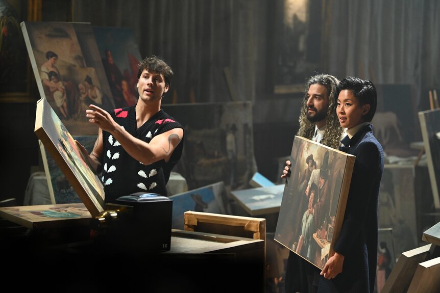 Rob Rausch, Mark Ballas, and Kristen Kish hold up paintings on The Traitors Episode 408.