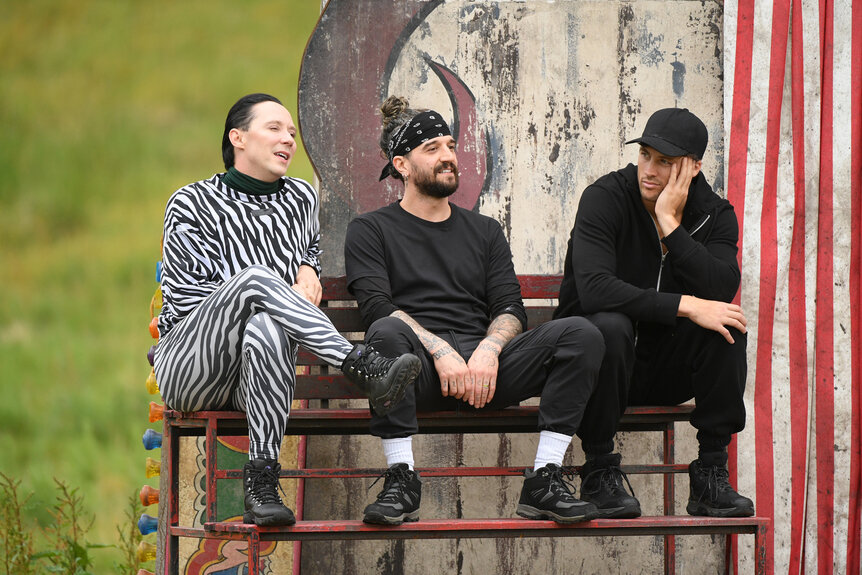 Johnny Weir, Mark Ballas, and Rob Rausch sitting on a bench during The Traitors Season 4 Episode 10.