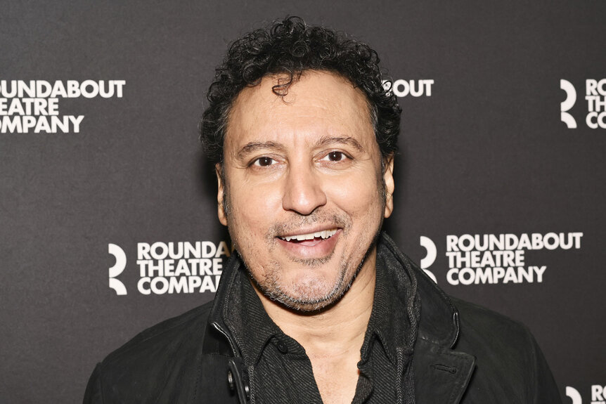 Aasif Mandvi posing in front of a step and repeat.