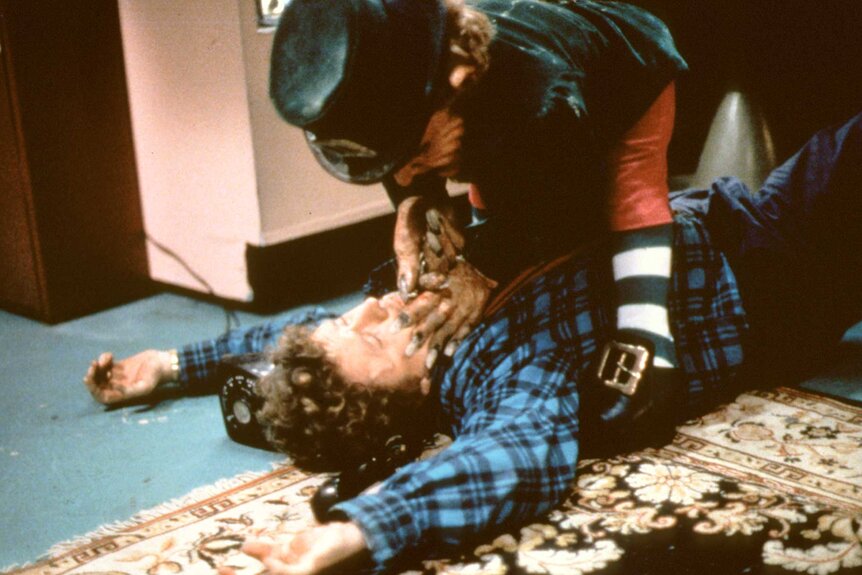 Leprechaun pinning someone down and covering their mouth in Leprechaun (1993).