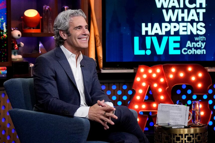 Andy Cohen wearing a suit sitting in a blue chair on Watch What Happens Live