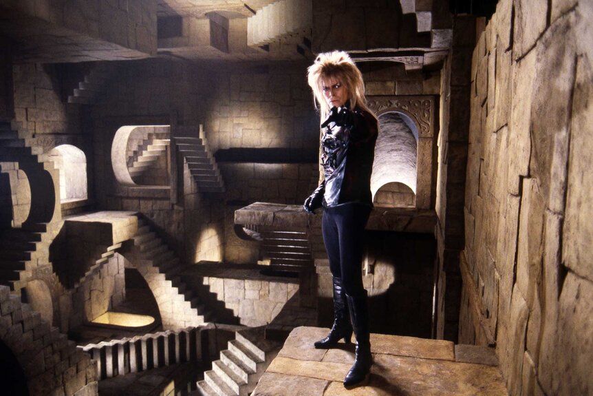Jareth walking through a room full of stairs in Labyrinth (1986).