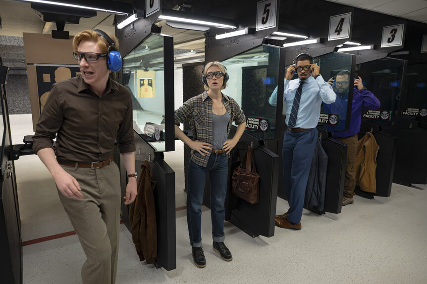Ned (Domhnall Gleeson), Mare (Chelsea Frei), Detrick (Melvin Gregg), and Travis (Eric Rahill) at a gun range in The Paper Season 2 Episode 4.