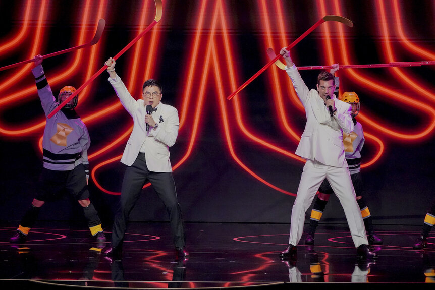 Bowen Yang and Matt Rogers performing on stage in black and white suits.