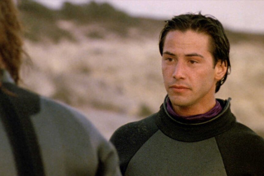 Johnny Utah talking to another person on the beach in Point Break (1991).