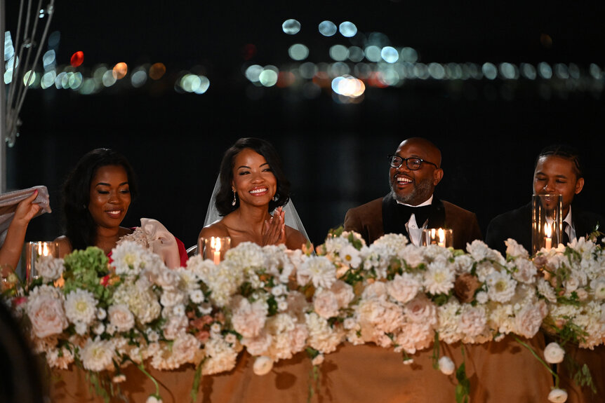 Nikki Jefferson and Shawn Best sitting at a table covered with flowers with their wedding party.