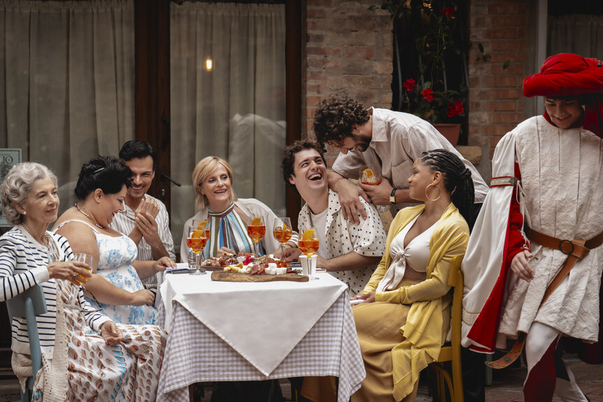 The cast of You, Me & Tuscany (2026) sitting and laughing around a dining table.