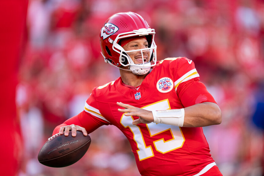 Patrick Mahomes passing a football to a team mate for practice on a football feild.