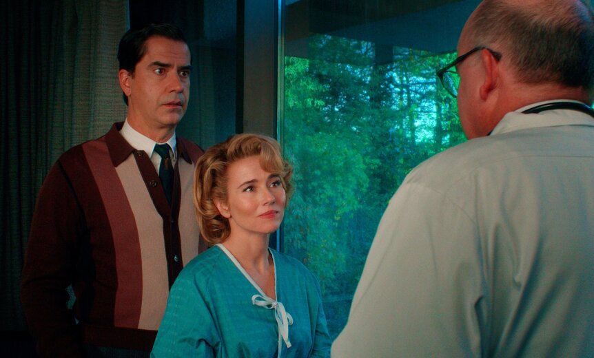 Hamish Linklater as Elias and Linda Cardellini as Pam Voorhees stand facing Jeffery Bean as Dr. Valentine in a room with large windows.