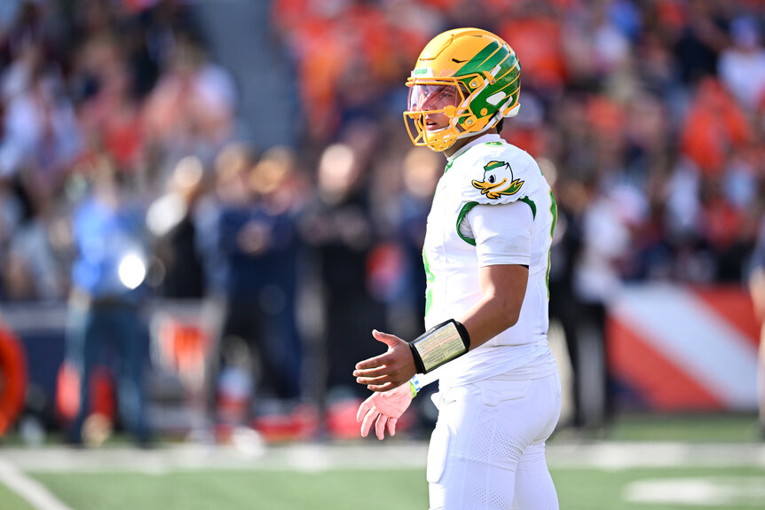 Oregon Ducks quarterback Dylan Raiola stands on the field in a white uniform and yellow helmet during a college football game.