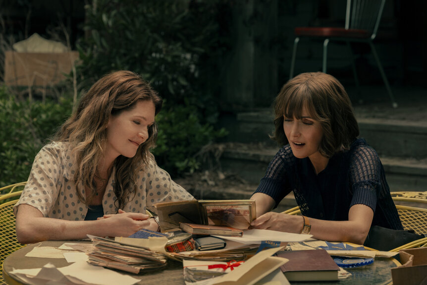 Meghann Fahy as Charlie and Rose Byrne as Sam looking at photos and old books on The Good Daughter Season 1.
